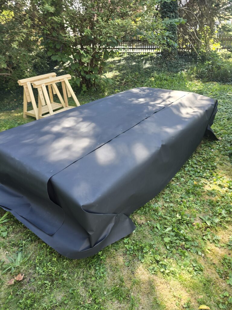 Dunkle Dachbahn auf einem liegenden Bauteil mit noch überstehenden Rändern.